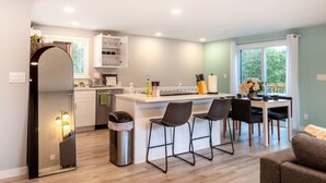 A modern kitchen with a central island, bar stools, and a dining area with a view of the outdoors. - Modern 5BR 3BA Remodeled Home with BBQ Backyard (Seattle)