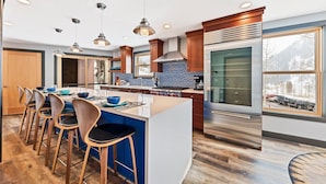 A modern kitchen with a central island, bar stools, a large refrigerator, and a window with a view of a parking lot. - Enjoy pure luxury in Alta in this Contemporary Condominium with Hot Tub (Alta)