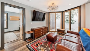 A modern living room with a large window, a wooden cabinet, a leather sofa, and a patterned rug. - Enjoy pure luxury in Alta in this Contemporary Condominium with Hot Tub (Alta)