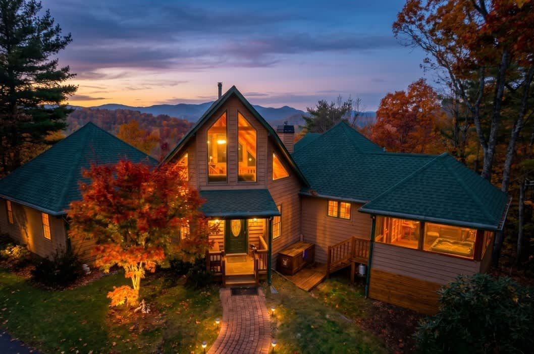 A cabin with a central main building and two smaller attached structures, surrounded by autumn foliage and a mountain backdrop.