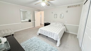 A bedroom with a bed, a desk, a chair, a mirror, a ceiling fan, and a door. - Comfort meets charm (Fayetteville)