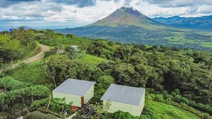 Un paysage rural avec une montagne en arrière-plan, deux bâtiments à toits plats et un chemin de terre.