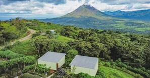 Un paisaje rural con una montaña al fondo, dos edificios con techos planos y un sendero de tierra.