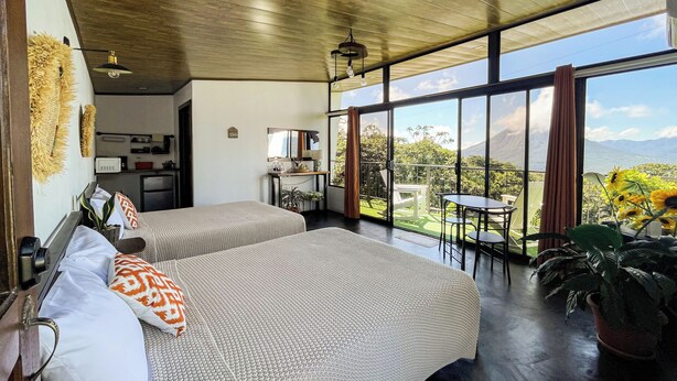 Une chambre avec deux lits, un coin repas comprenant une table et des chaises, et une grande fenêtre donnant sur l’extérieur.