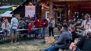 An outdoor gathering with a rustic wooden building, a sign advertising cold beer and live music, and a mountainous backdrop. - Anvil Room Rustic Stay at Columbine Lodge (Silverton)
