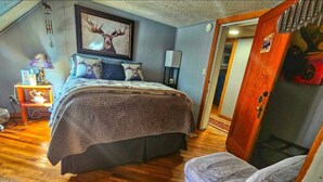 A bedroom with a large bed, a chair, a wooden floor, and a door leading to another room. - Anvil Room Rustic Stay at Columbine Lodge (Silverton)