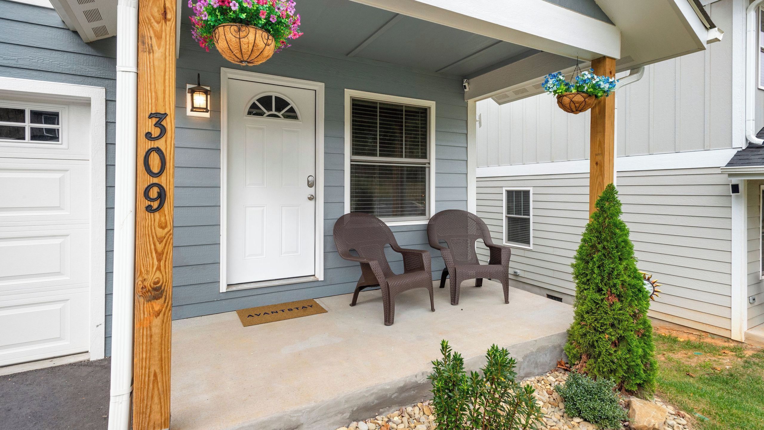 A house with a porch, a door marked '309', two wicker chairs, and a small potted plant.