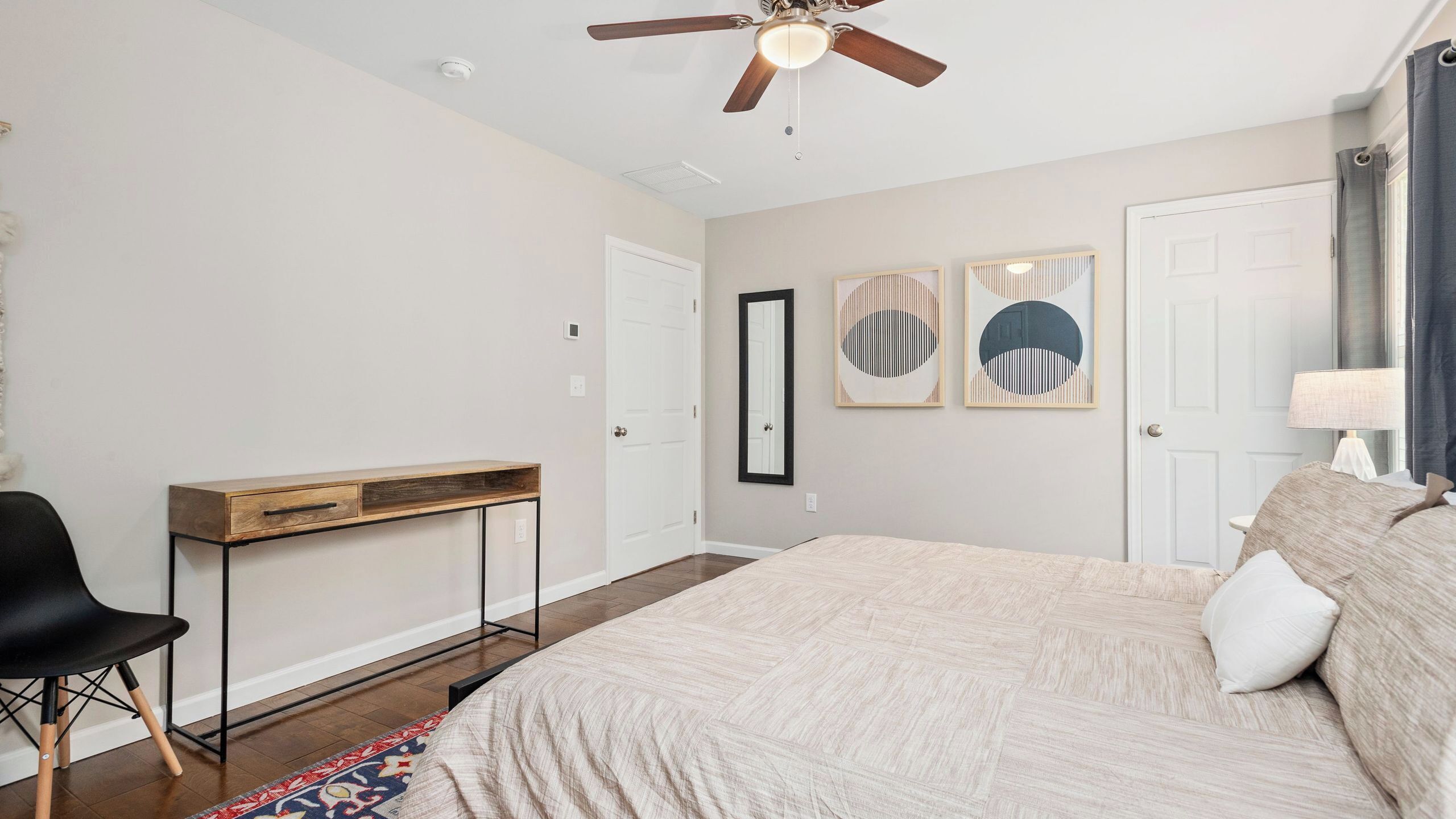 Ein Schlafzimmer mit Bett, Schreibtisch, Stuhl, Deckenventilator und Bildern an der Wand.