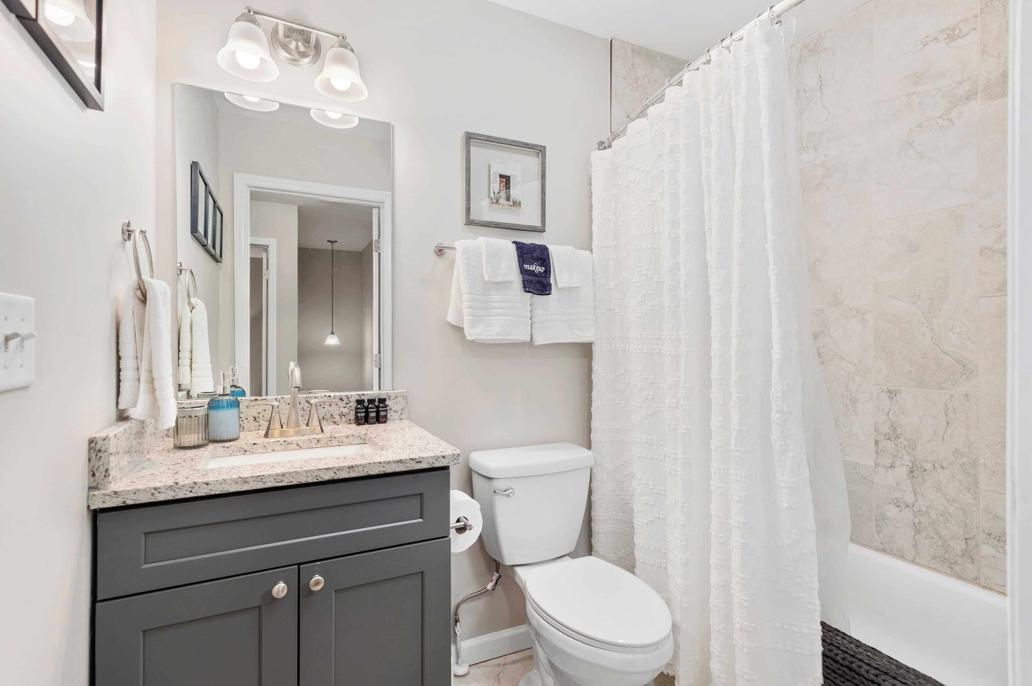 A bathroom with a white toilet, a sink with a marble countertop, a mirror, and a shower curtain.