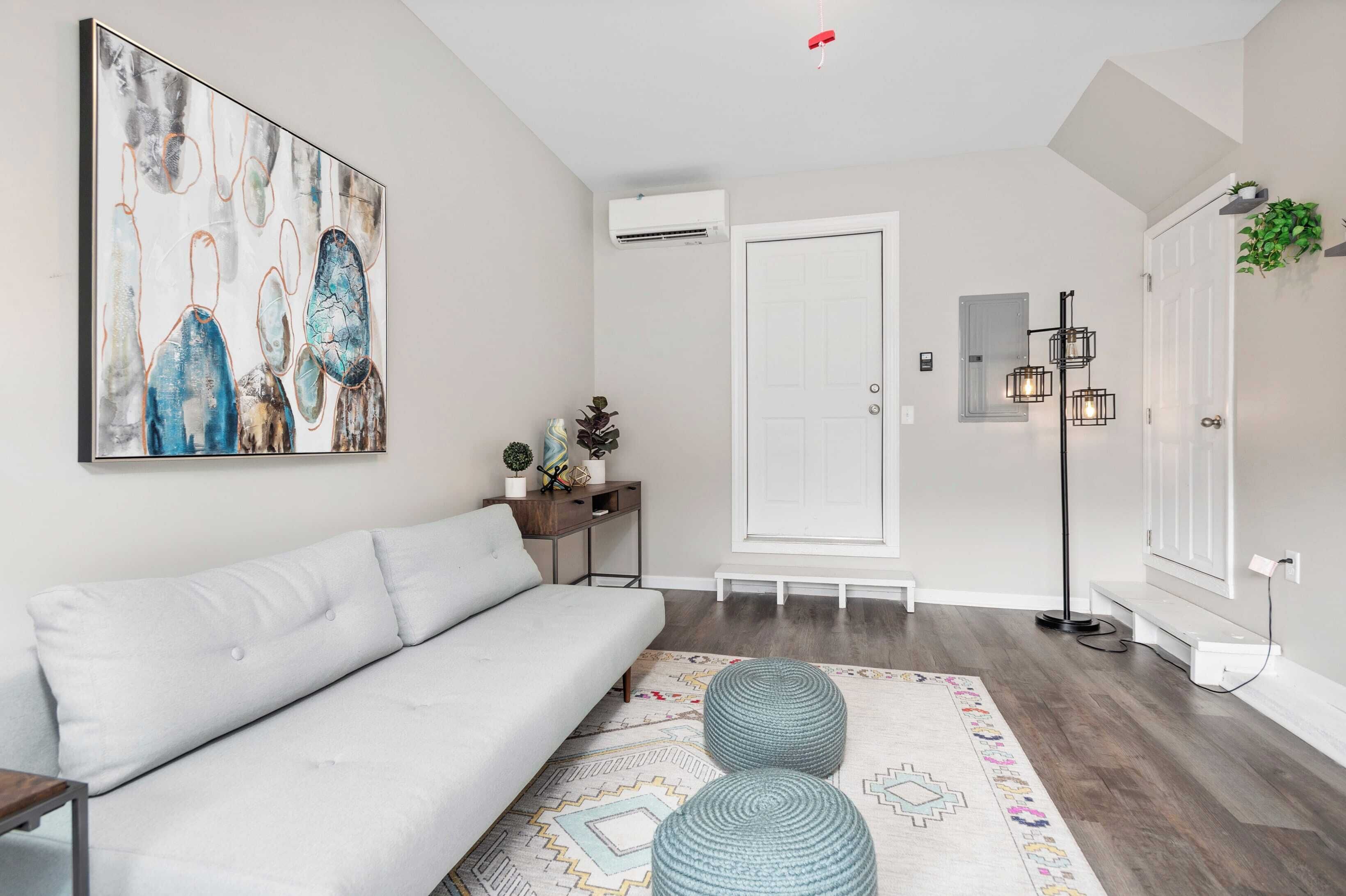 A modern living room with a white sofa, a colorful rug, and a large abstract painting on the wall.