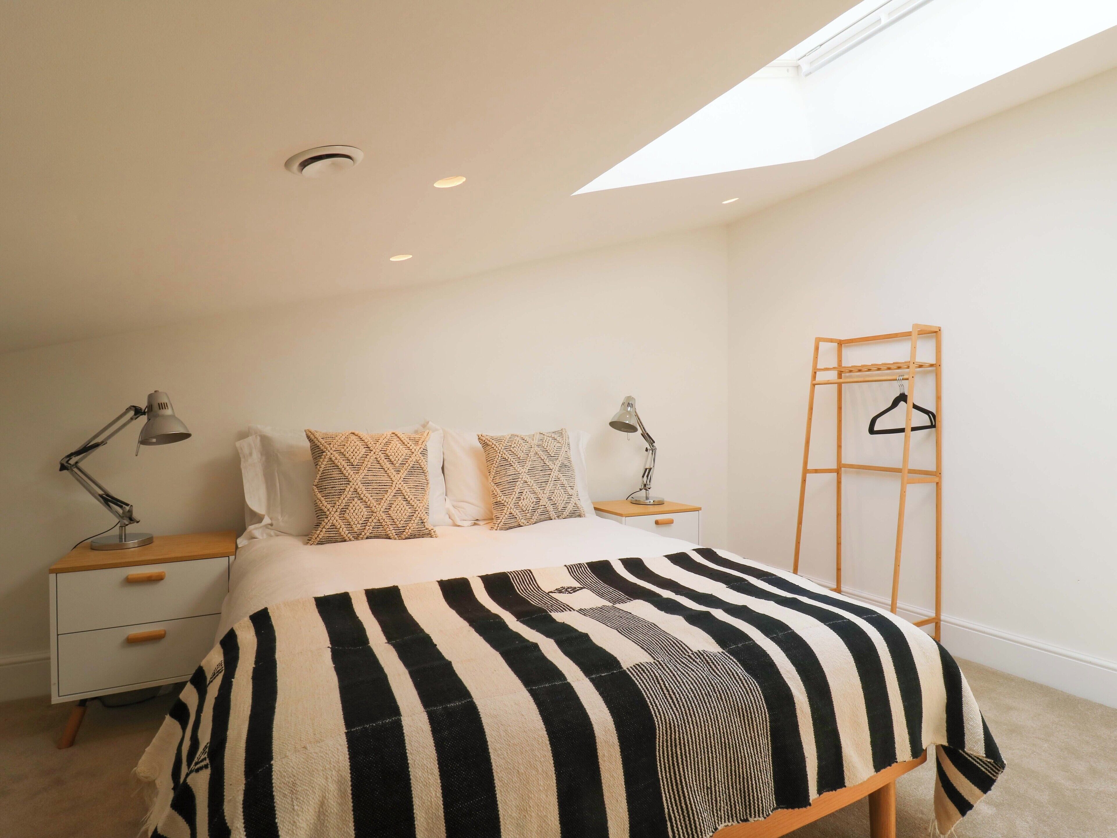 A bedroom with a bed, two bedside tables with lamps, a wooden ladder, and a ceiling light.