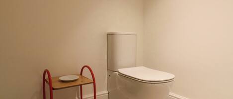 A small bathroom with a white toilet, a wooden shelf with a red frame, and a patterned container.