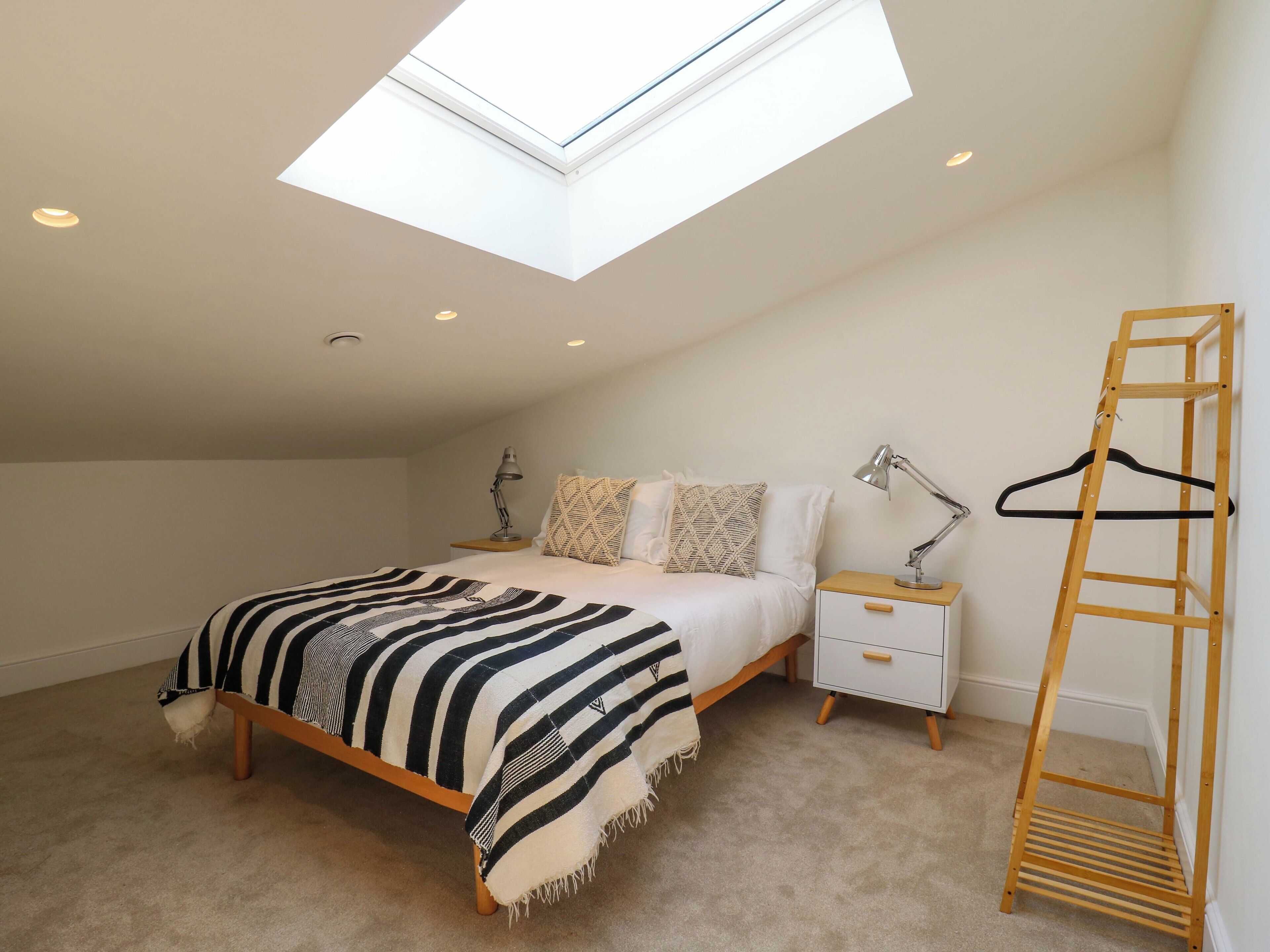 A bedroom with a skylight, a bed with a striped blanket, bedside tables with lamps, and a wooden ladder.