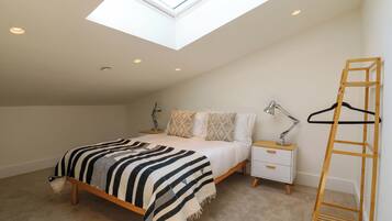 A bedroom with a skylight, a bed with a striped blanket, bedside tables with lamps, and a wooden ladder.