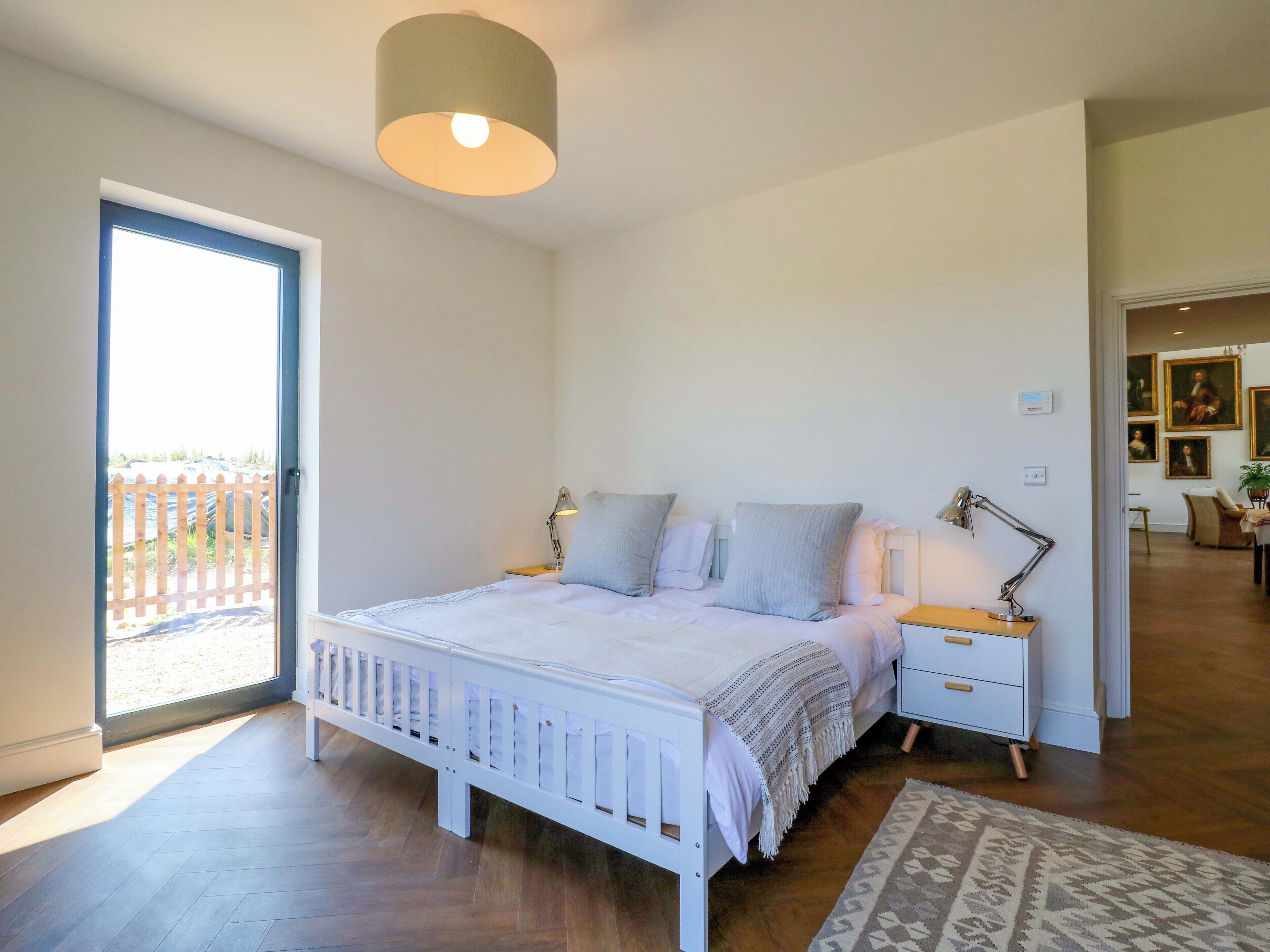Habitació amb un llit, taules de nit, una làmpada, una vista per una porta i una catifes amb dibuixos.