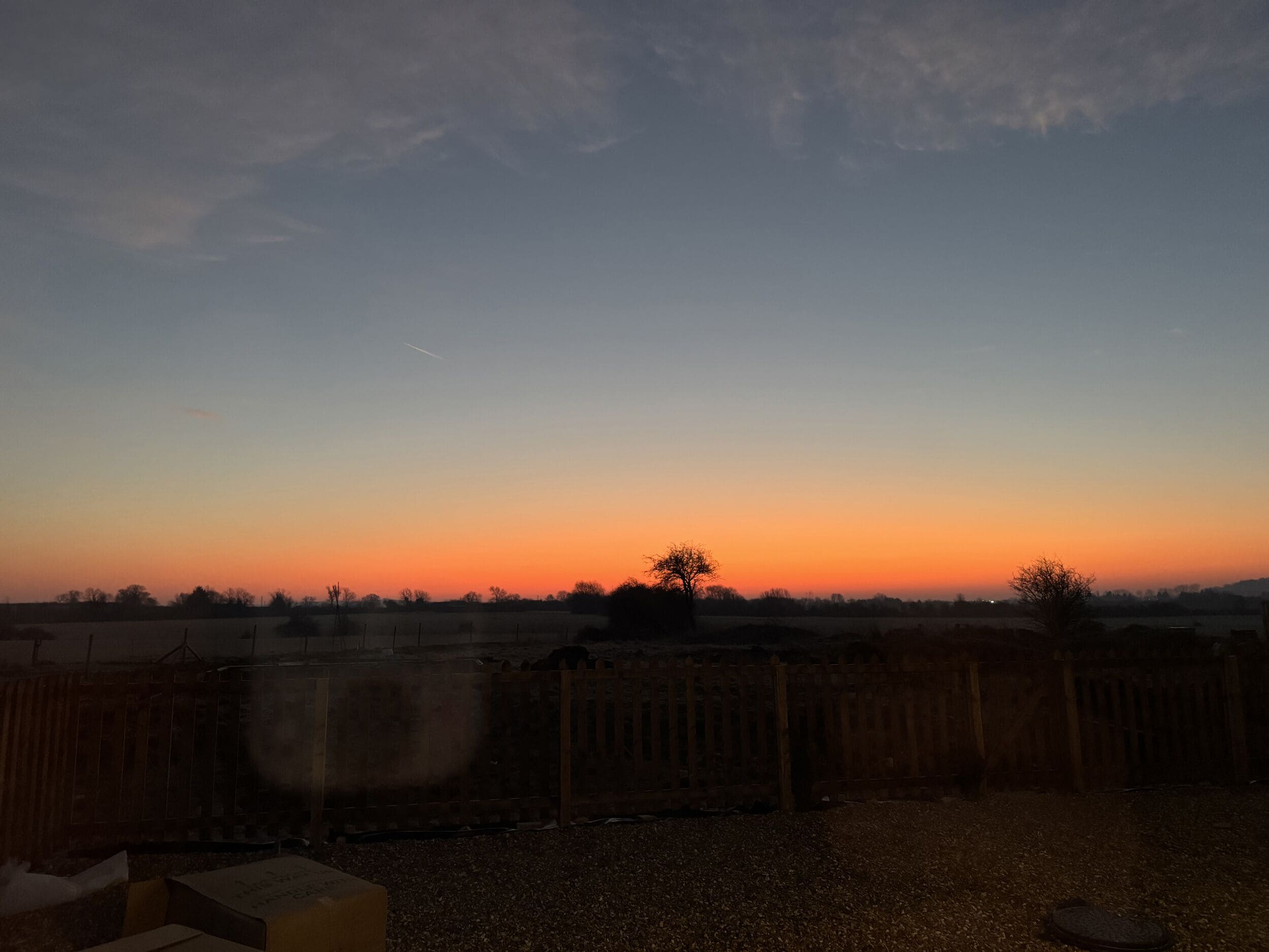 Une vue sur le coucher de soleil depuis un balcon, avec une clôture en bois au premier plan.