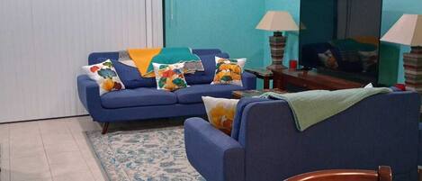 A living room with a blue sofa set, a dining table, and a TV.