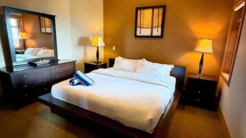 Une chambre d’hôtel avec un grand lit, deux tables de chevet avec des lampes, une commode, un miroir et un tableau encadré au mur.