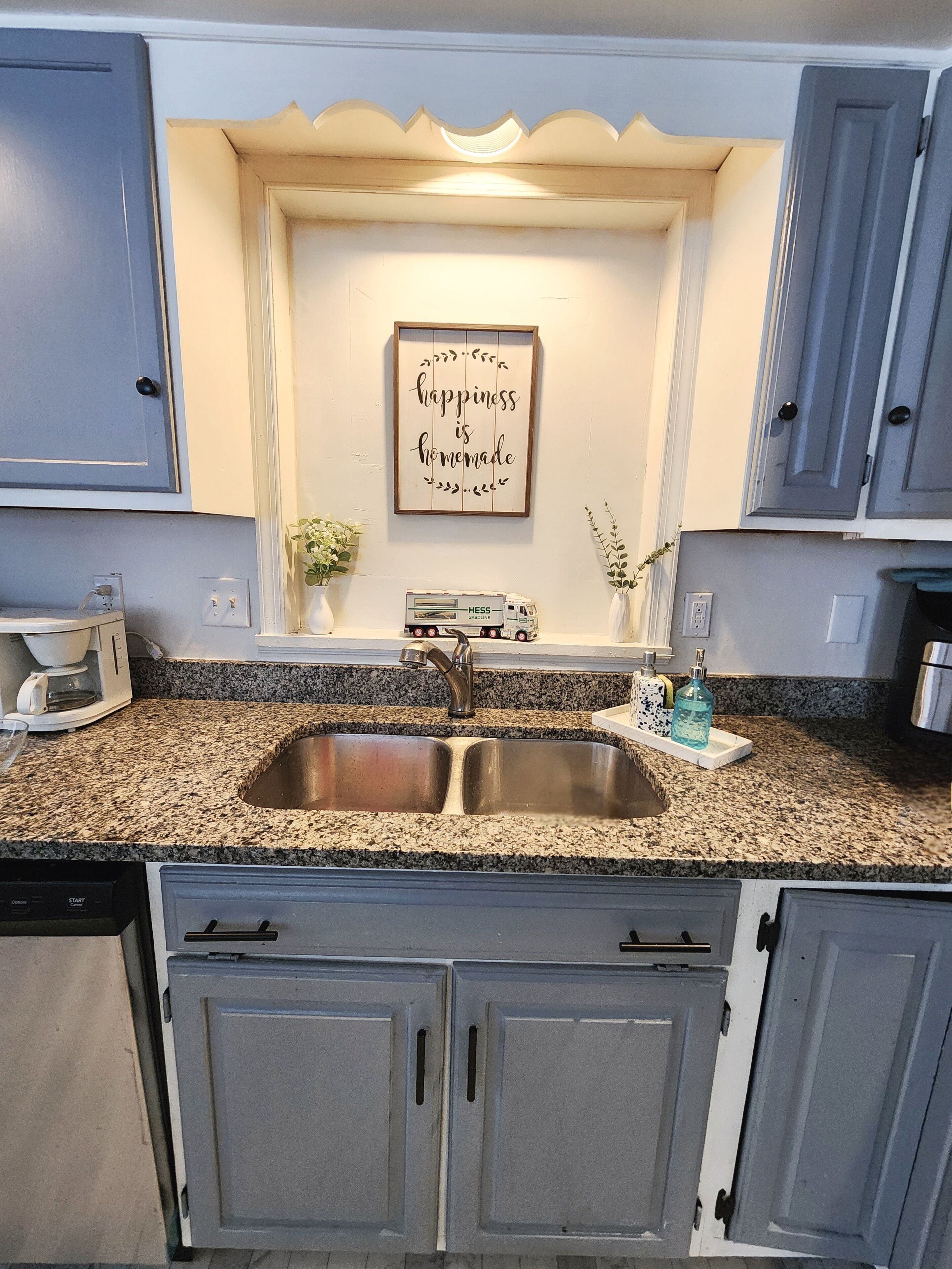 A kitchen with a granite countertop, stainless steel sink, and a decorative sign above the sink.