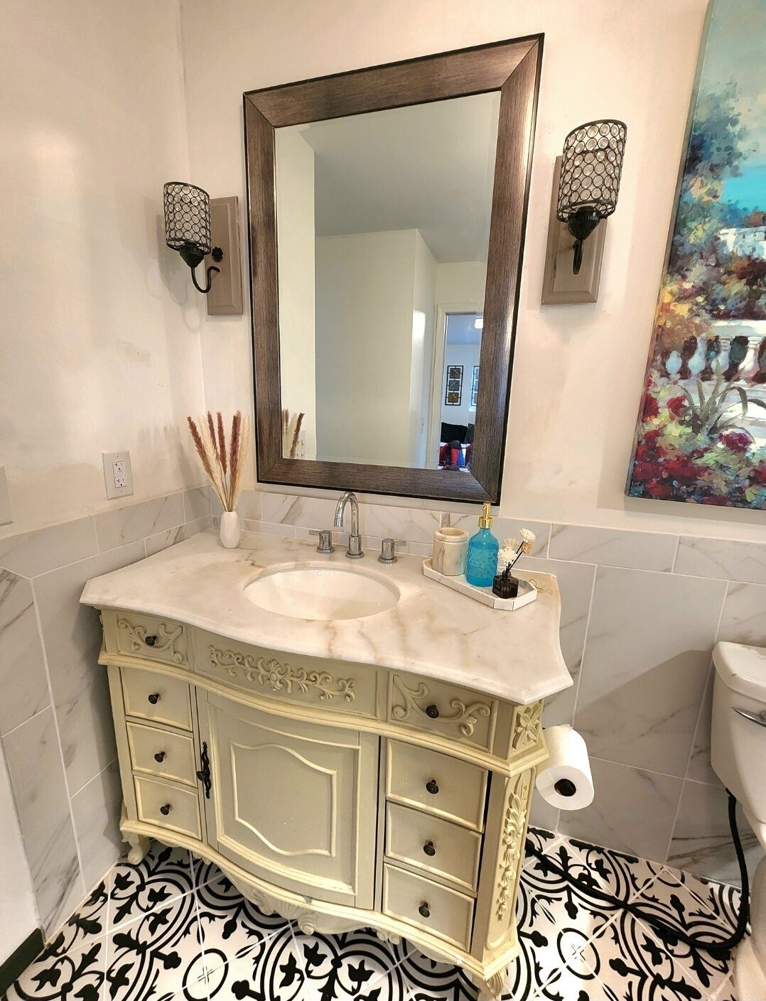 A bathroom with a marble sink, a large mirror, wall sconces, and a patterned floor.