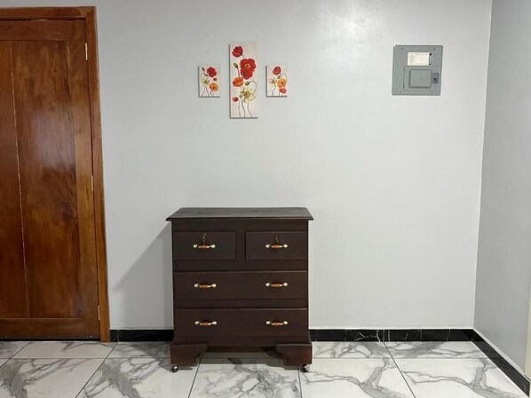 A room with a wooden door, a dark brown dresser with multiple drawers, and three floral paintings on the wall.