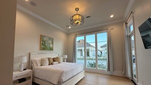 A bedroom with a large bed, a nightstand, a lamp, a painting, and a view of the outside. - The Kentwood- A Luxury Home in Baton Rouge- minutes from LSU and downtown! (Baton Rouge)