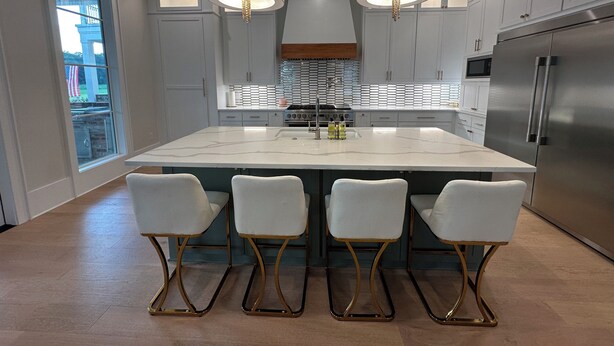 A modern kitchen with a large island, white bar stools, stainless steel appliances, and pendant lighting. - The Kentwood- A Luxury Home in Baton Rouge- minutes from LSU and downtown! (Baton Rouge)