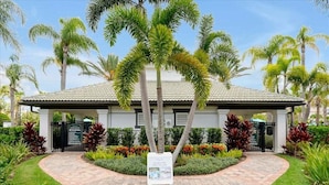 A hotel entrance with a paved pathway, palm trees, and a signboard.