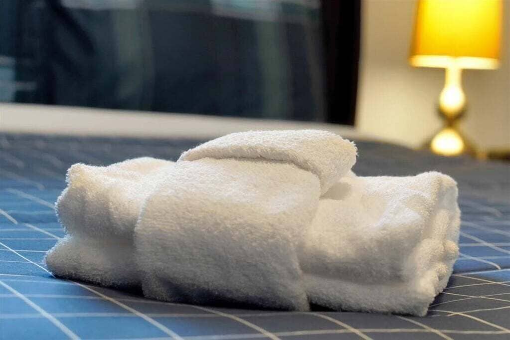 A neatly folded white towel on a bed with a blue patterned bedspread.