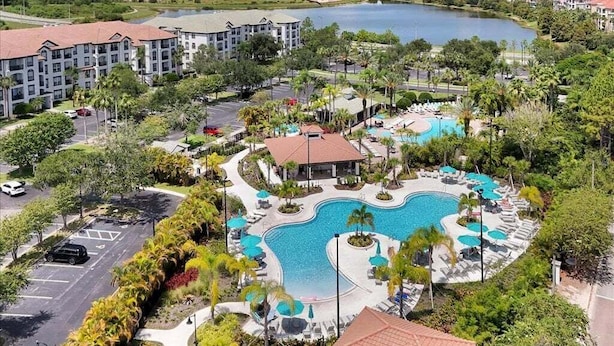A resort with a large swimming pool, multiple lounge areas, and a view of a lake.