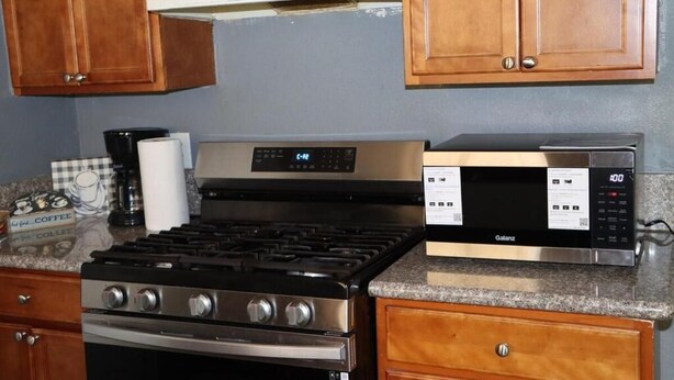 A kitchen with a gas stove, oven, microwave, and wooden cabinets. - Spacious 2-Bedroom Retreat in San Jacinto; Sleeps 6, AC & Pet-Friendly (San Jacinto)
