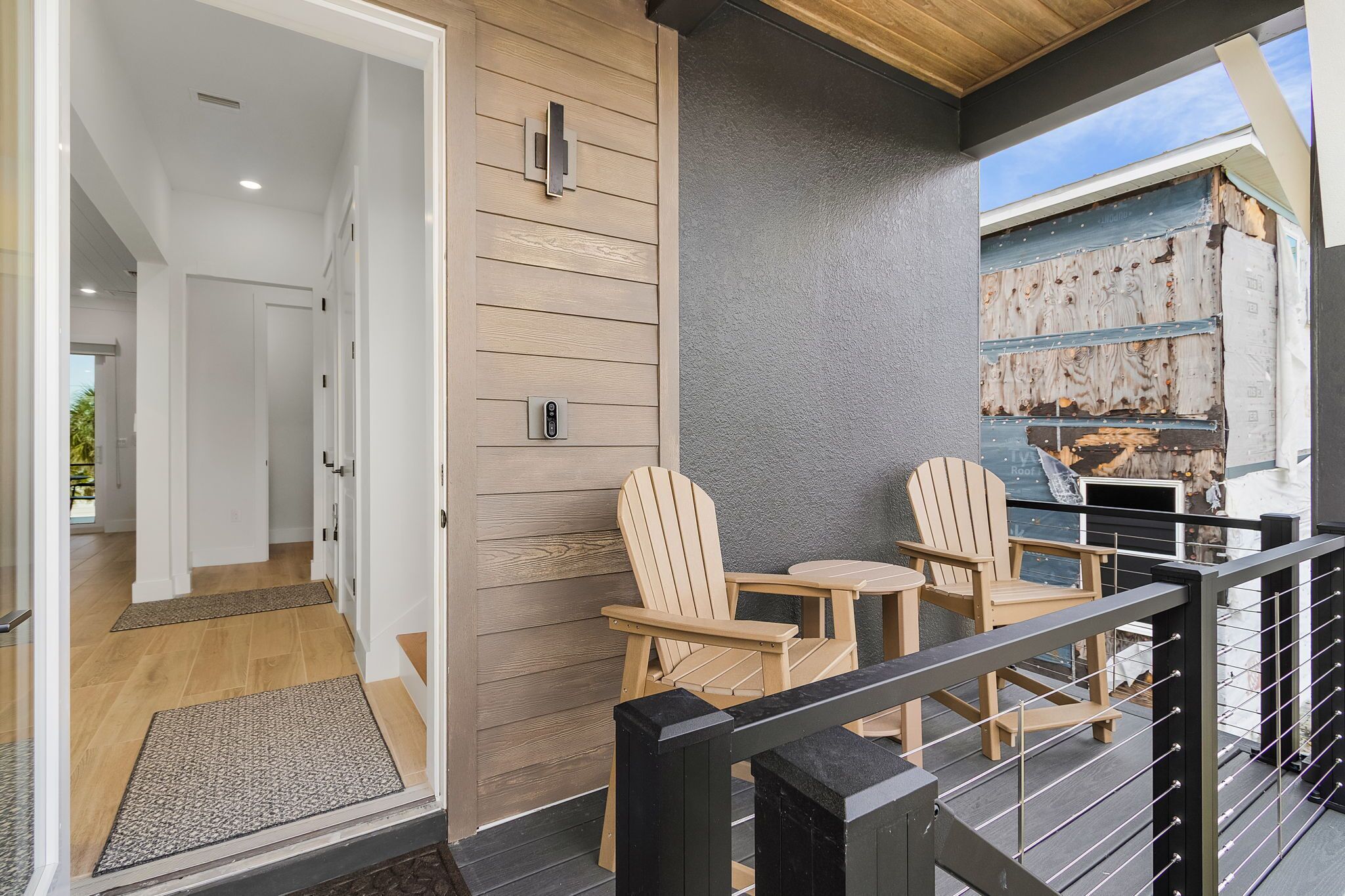 A modern interior with a wooden wall, a balcony with Adirondack chairs, and a view of a rustic building.