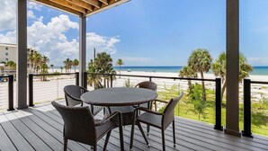 Un espace extérieur abrité, doté d’une table et de chaises, qui offre une vue sur une plage bordée de palmiers et un ciel dégagé.