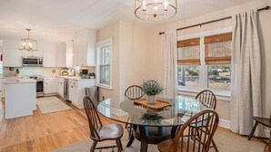 A modern kitchen with white cabinetry, a central island, and a dining area with a glass table and wooden chairs. - The Park Circle Haven ~ Spacious 5br/4ba Home! (North Charleston)