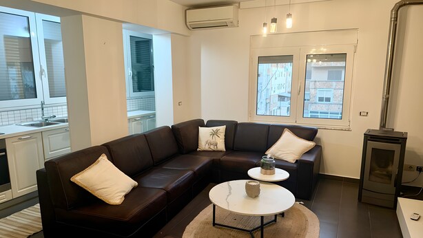 A modern living room with a brown leather sectional sofa, a round coffee table, and a small side table. - Cozy 2-bedroom apartment in center Durres (durres)