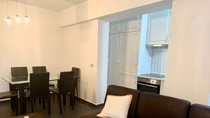 A modern living room with a brown leather sofa, a glass dining table with four chairs, and a kitchen area with white cabinets and a stove. - Cozy 2-bedroom apartment in center Durres (durres)
