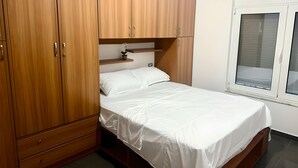 A bedroom with a bed, wooden wardrobe, and a window. - Cozy 2-bedroom apartment in center Durres (durres)