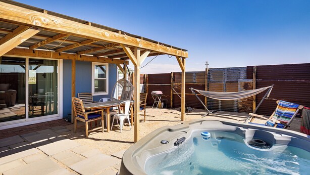 Un patio trasero con jacuzzi, mobiliario de exterior y un pérgola.
