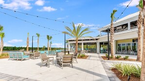 Une terrasse extérieure aménagée avec des sièges et un espace piscine, le tout entouré de palmiers et d’un bâtiment doté de grandes fenêtres.