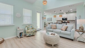 Un salon spacieux avec un canapé bleu clair, un pouf en osier et un coin repas avec une cuisine en arrière-plan.