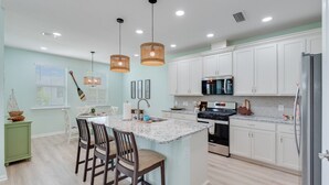 Une cuisine moderne avec des meubles blancs, un îlot central doté de tabourets et des luminaires suspendus.