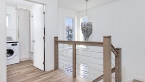 Een net appartement in moderne stijl, met een houten trap, een wasmachine en een hanglamp.