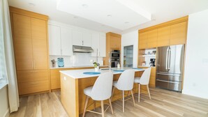 Een moderne keuken met houten kastjes, een roestvrijstalen koelkast en een centraal kookeiland met stoelen.