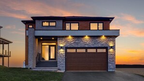 Een modern huis met twee verdiepingen, een stenen gevel, een ruime garage en een goed verlichte entree.