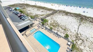 A swimming pool with lounge chairs and a deck area, overlooking a beach with umbrellas and sun loungers. - BEACH FRONT, FAMILY FRIENDLY, WALK TO THE HANGOUT! | BEACHBALL PROPERTIES (Gulf Shores)