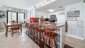 A modern kitchen with white cabinets, a granite countertop, and a bar area with wooden stools. - BEACH FRONT, FAMILY FRIENDLY, WALK TO THE HANGOUT! | BEACHBALL PROPERTIES (Gulf Shores)