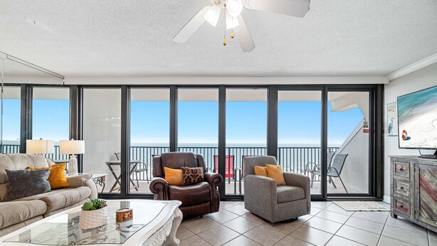 A spacious living room with a large window, a ceiling fan, and a view of the ocean. - BEACH FRONT, FAMILY FRIENDLY, WALK TO THE HANGOUT! | BEACHBALL PROPERTIES (Gulf Shores)