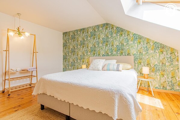 A bedroom with a bed, a wooden ladder, a floral wallpaper, and a skylight.