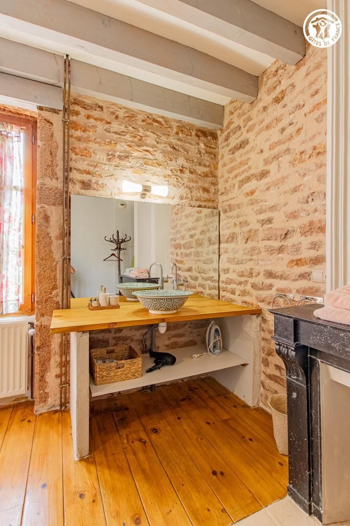 Une salle de bain rustique avec un mur en pierre, un meuble-lavabo en bois et un miroir.