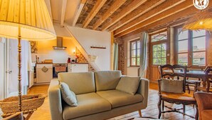 Un interior acogedor con sofá, mesa de comedor, sillas, vigas de madera en el techo y una cocina al fondo.